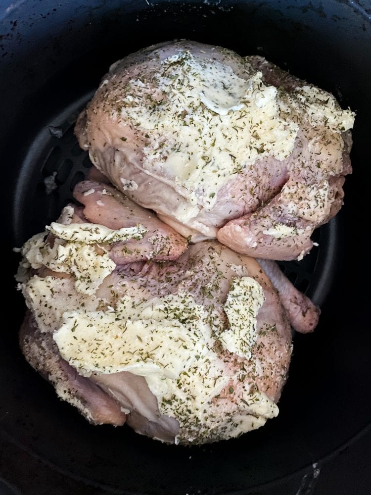 raw cornish game hens in an air fryer basket with butter and seasonings