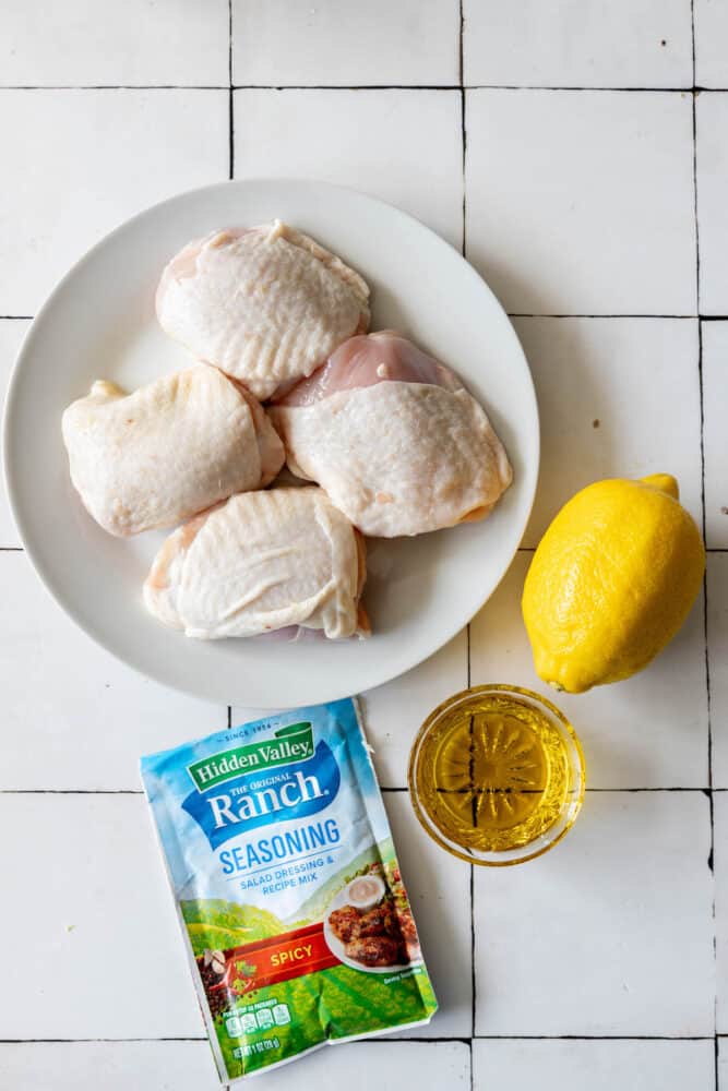 Chicken breasts on a plate next to lemons and a packet of ranch seasoning.