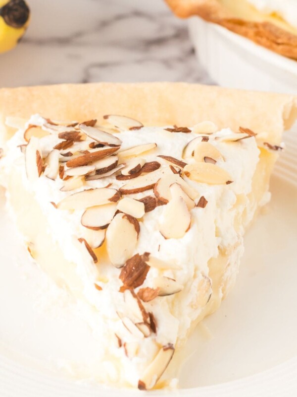 slice of banana cream pie with whipped topping and sliced almonds on top on a white plate