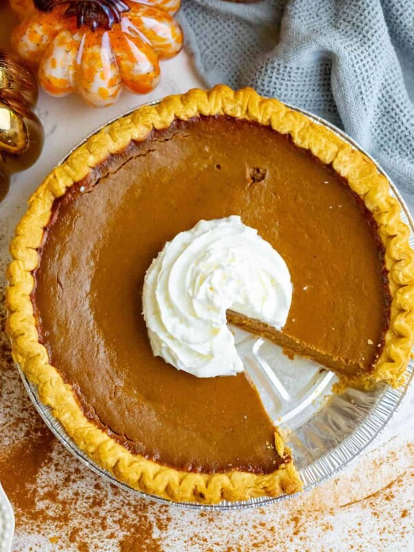 A spicy pumpkin pie with whipped cream and a slice taken out.