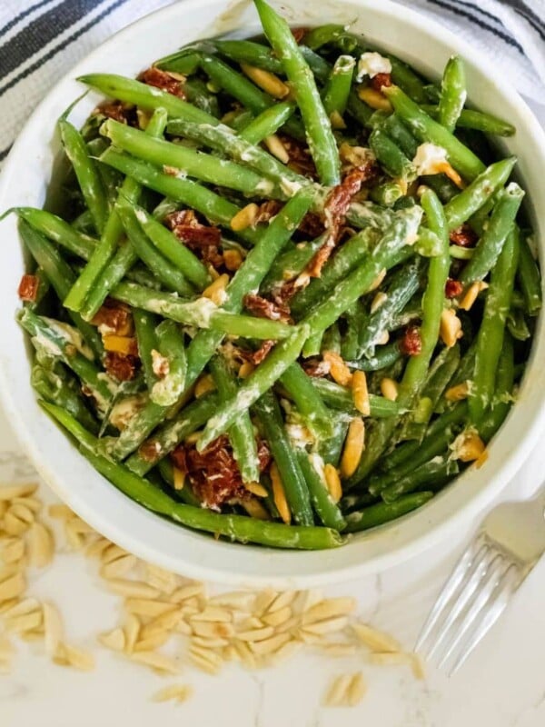 Cheesy green beans baked with sun-dried tomatoes in a white bowl.