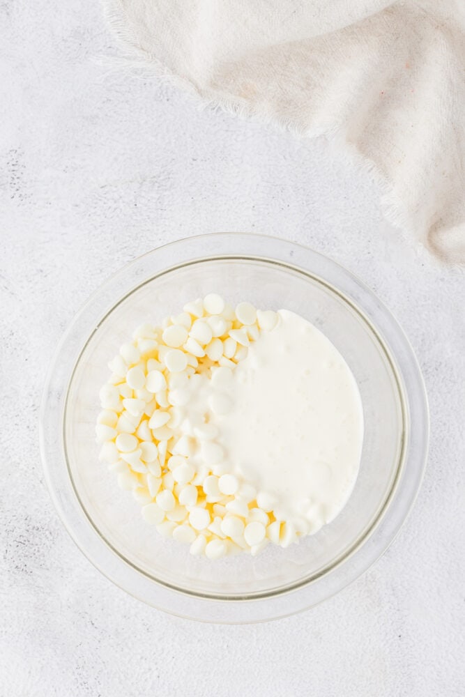 White chocolate chips in a glass bowl on a white background.