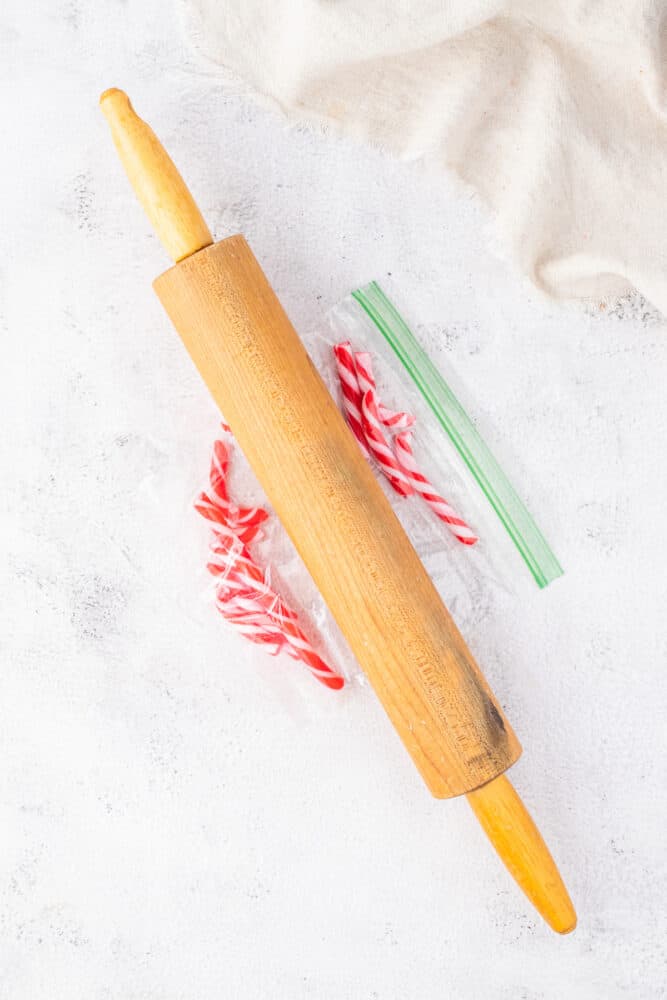 A rolling pin and candy canes sitting on a white surface.
