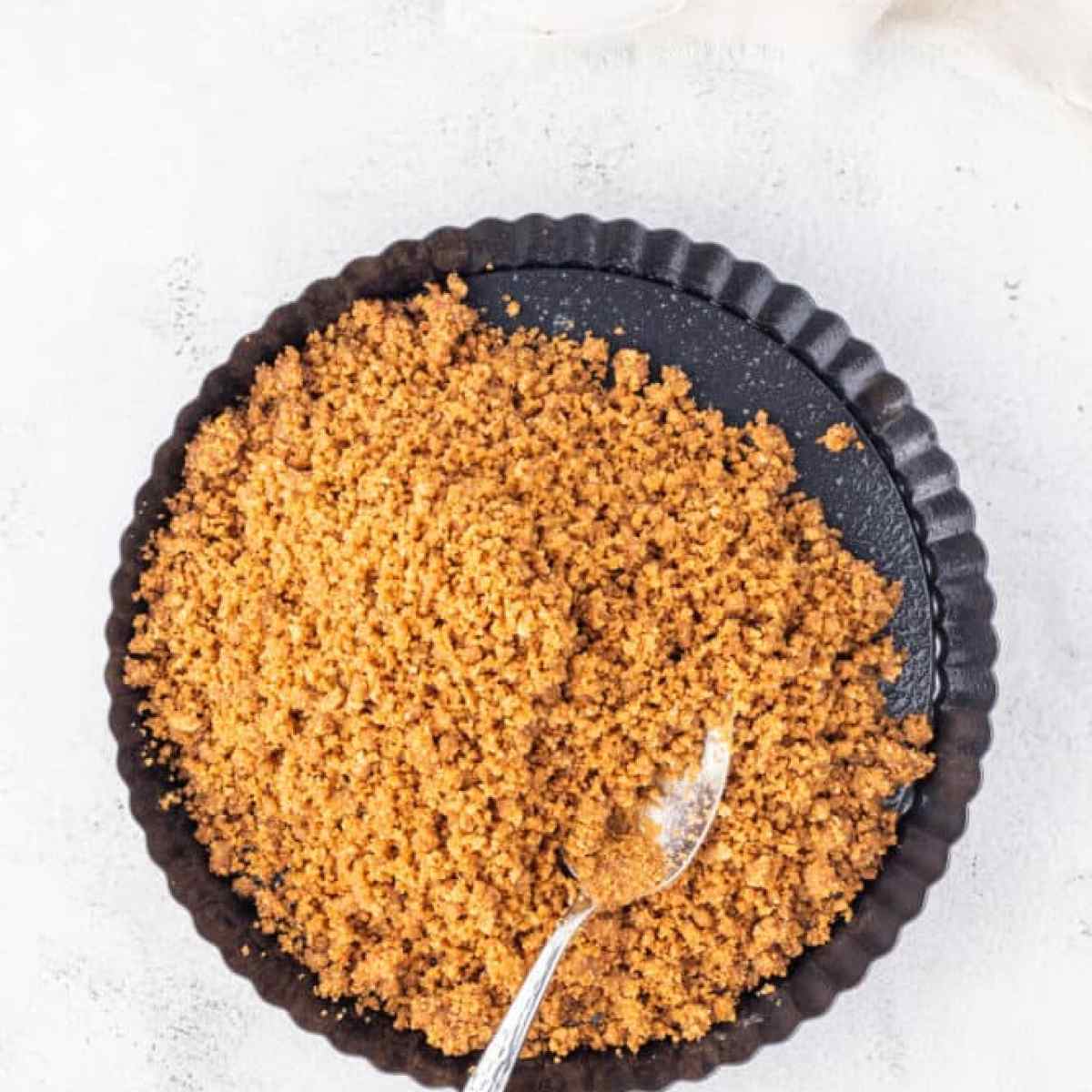 A bowl of brown sugar with a spoon on top, alongside an eggnog tart.