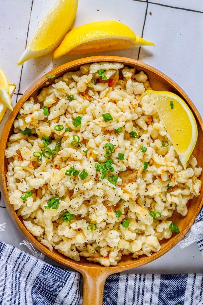 spaetzle in a wooden dish with a slice of lemon and sliced green onions on top