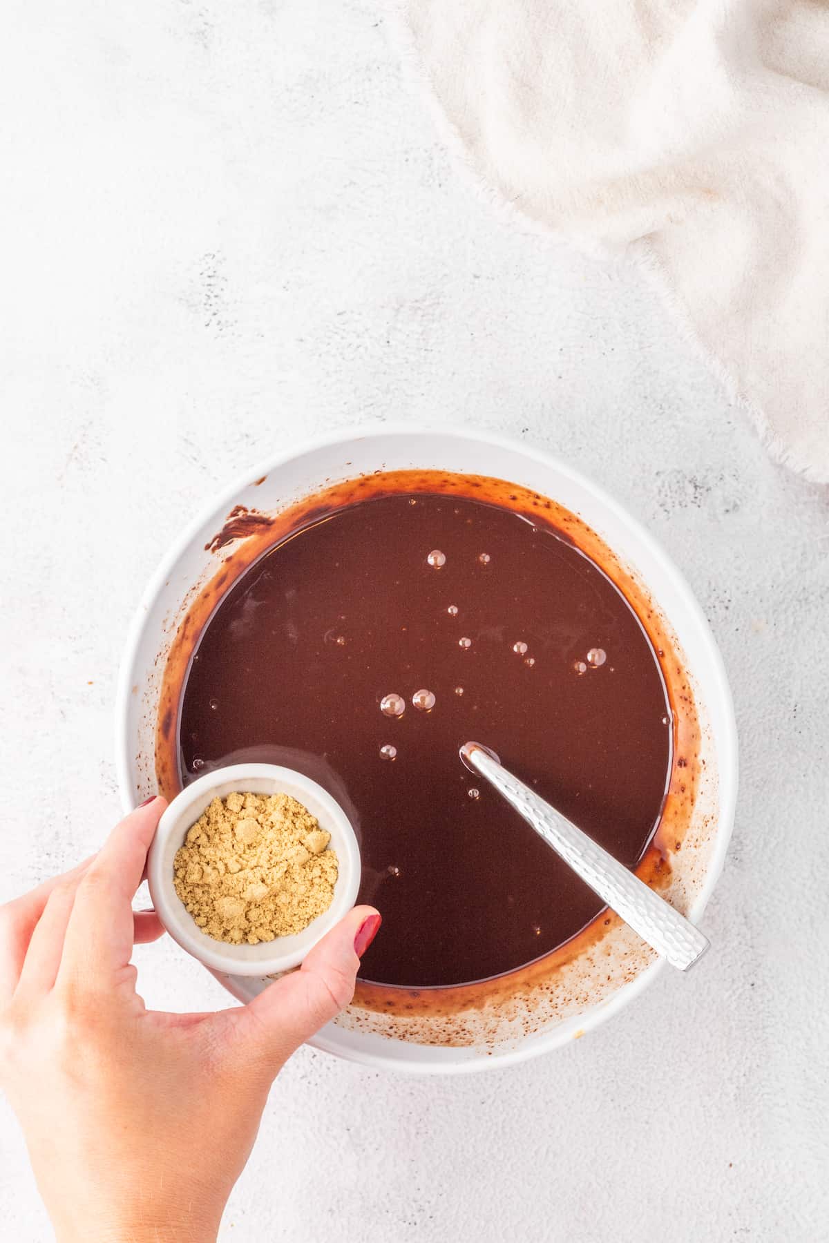 A person holding a bowl of chocolate sauce, preparing a Gingerbread Chocolate Caramel Tart Recipe.