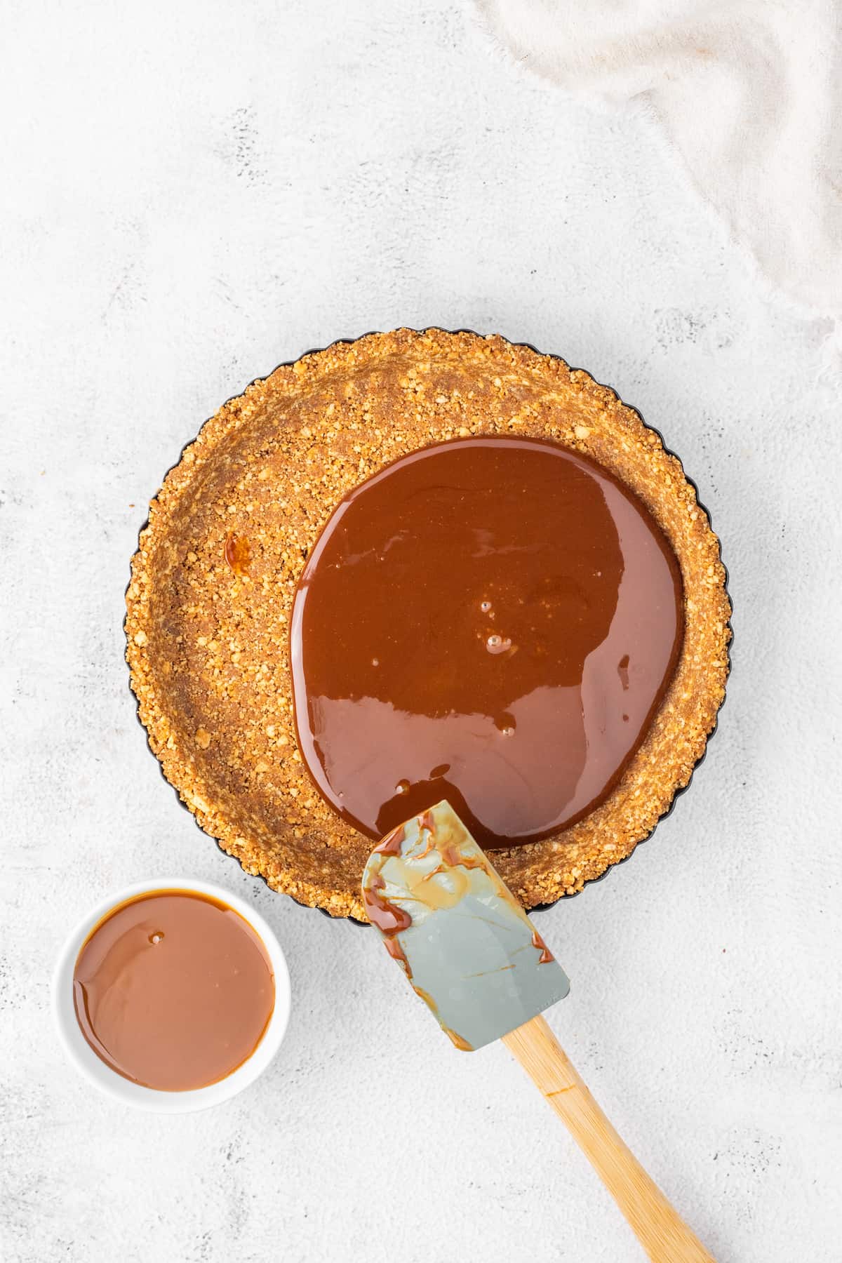 A delightful gingerbread chocolate tart drizzled with rich caramel sauce, accompanied by a handy spoon for easy enjoyment.
