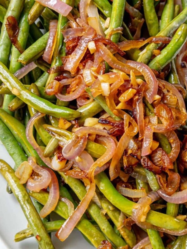 Sautéed green beans and red onion on a white plate.