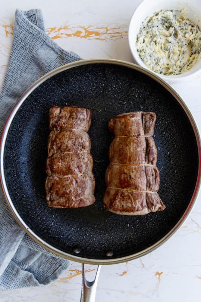 Two garlic herb beef tenderloin steaks in a frying pan with a sauce.