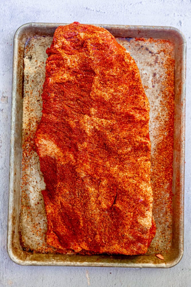 a raw seasoned brisket on a baking sheet
