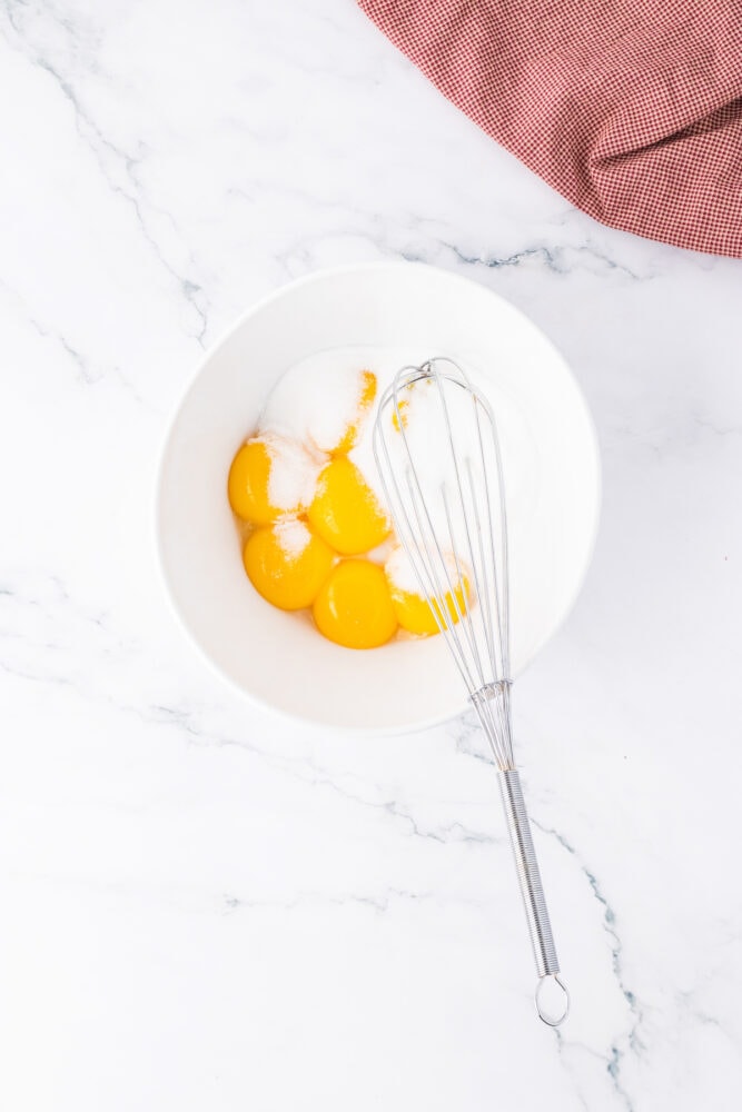 egg yolks, sugar, and a whisk in a bowl 