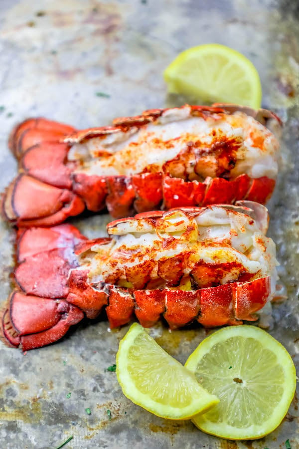 two broiled lobster tails on a baking sheet with lemon wedges