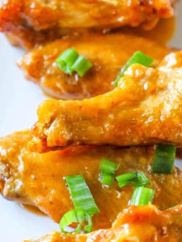 chicken wings in sauce on a plate with chopped scallions