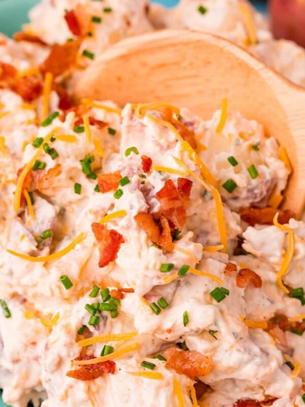 creamy ranch potato salad with chopped chives and crumbled bacon being scooped with a wooden spoon