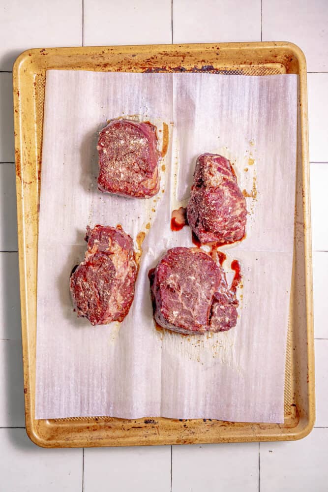 Four reverse sear filet mignon steaks on a tray on a tiled floor.