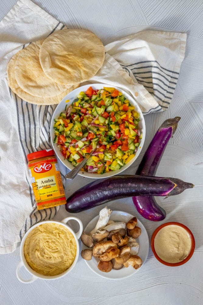 amba sauce, tahini, hummus, eggplant, israeli salad, pita, mushrooms on a table