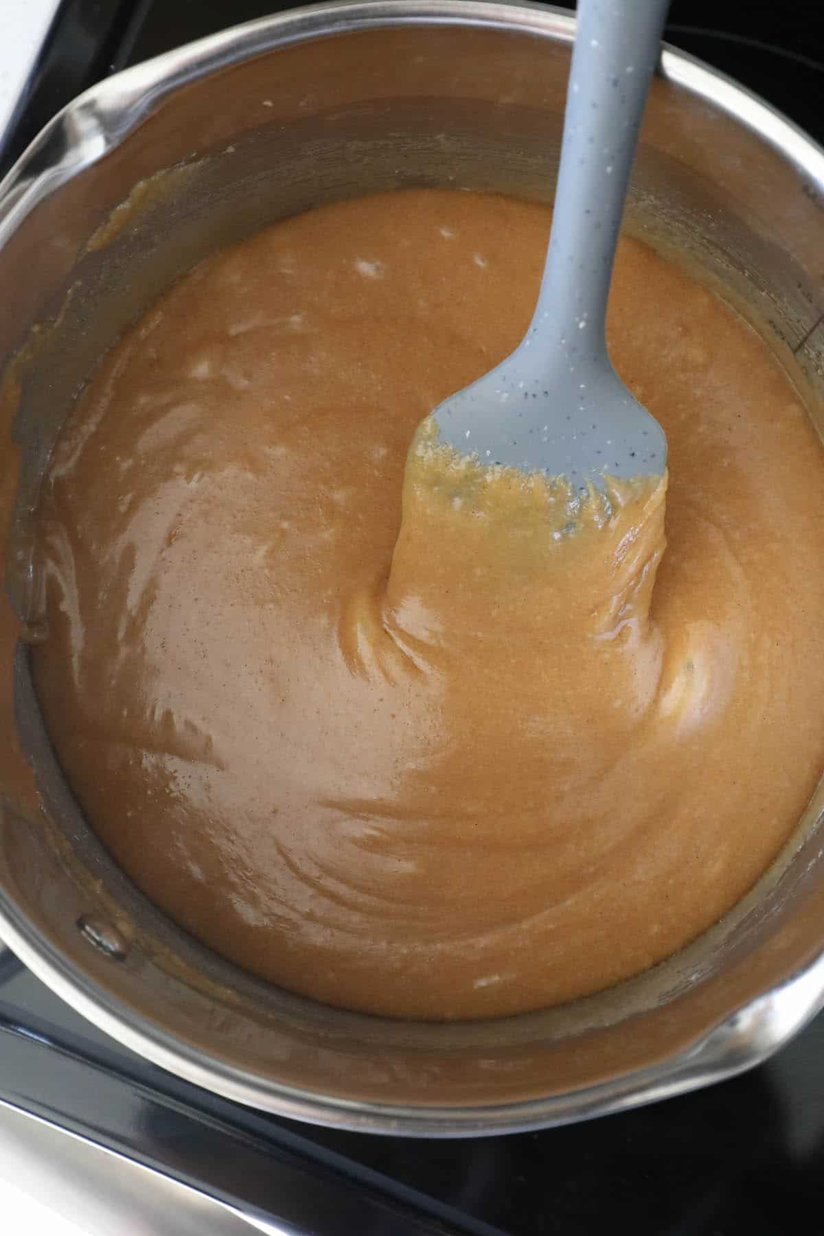 A brown sauce in a pan being stirred with a spatula, resembling the texture of scotcheroos.