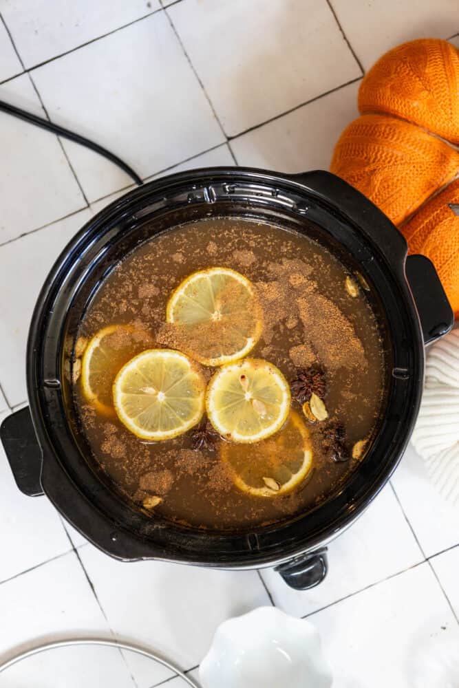 A crock pot filled with orange slices and pumpkins simmering slowly.
