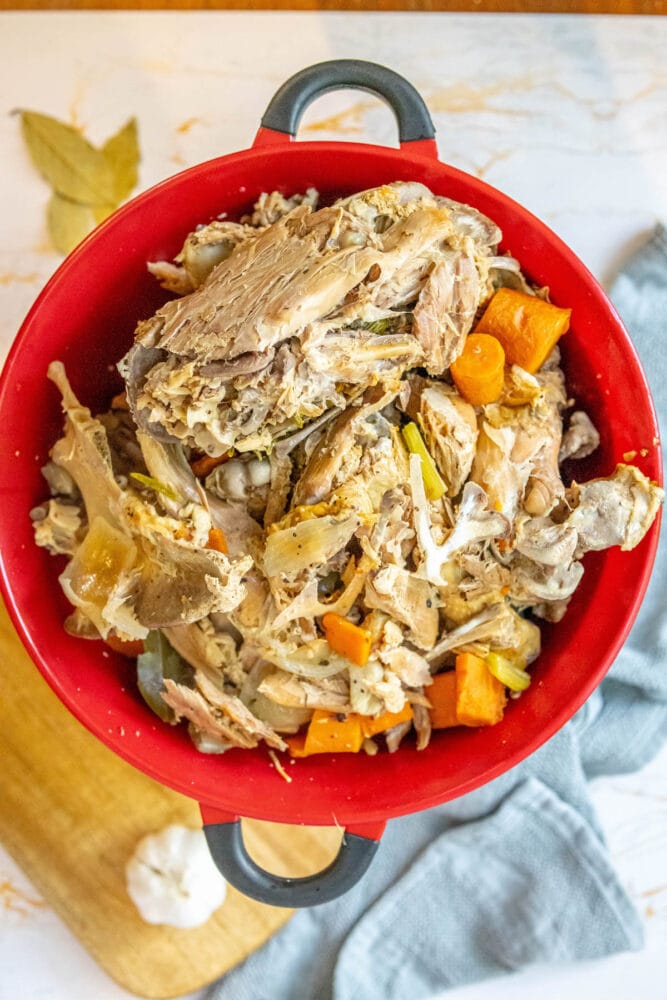 colander over a bowl with turkey carcass and cooked vegetables