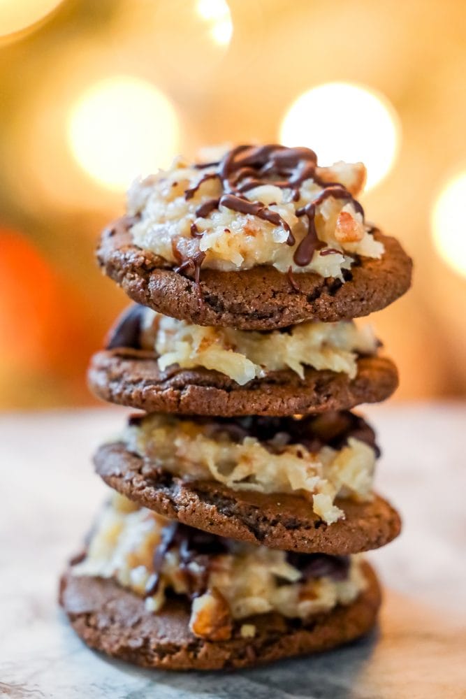 chocolate cookies covered in coconut and nut mixture and a drizzle of chocolate stack of them