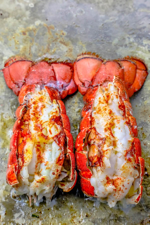 broiled lobster tails on a baking sheet topped with melted butter and a dash of paprika
