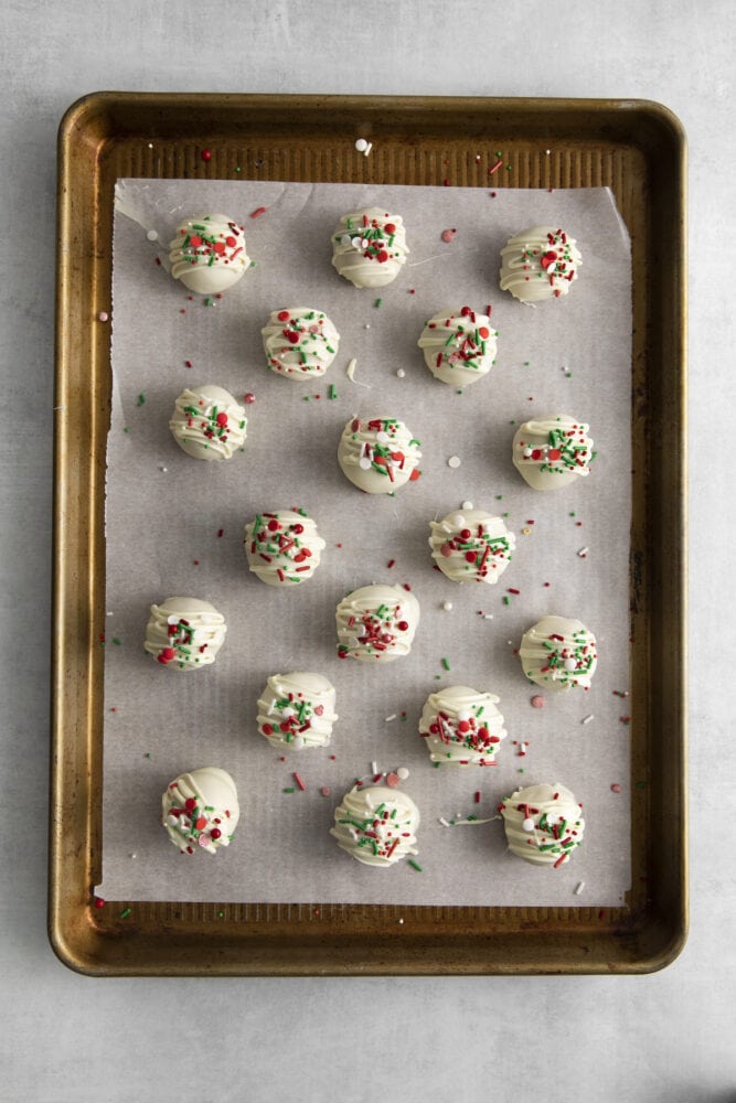 picture of peanut butter truffles dipped in white chocolate and topped with christmas sprinkles on a baking sheet lined with parchment paper